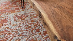 Een woonkamer met een houten salontafel, een leren fauteuil, een blauwe bank en een kamerkleed met een patroon.
