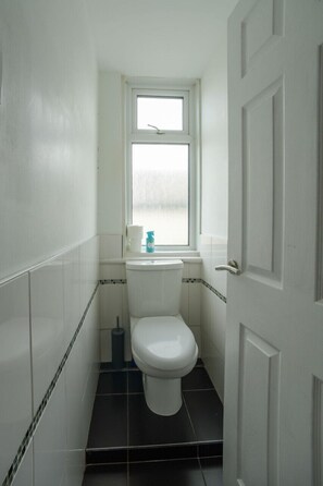 A small, white bathroom with a toilet, a window, and a door. - The Bells HOT TUB on Private Terrace Apartments (Blackpool)