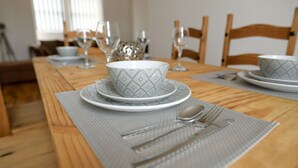 Une table à manger dressée avec un saladier à motifs, des assiettes, des couverts et un set de table.
