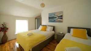 Une chambre avec deux lits, une fenêtre, un tableau et un vase de fleurs.