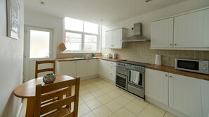 Une cuisine avec des meubles blancs, un plan de travail en bois, une cuisinière, un four, un four à micro-ondes et une fenêtre qui laisse entrer la lumière naturelle.