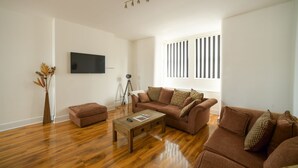 Un salon moderne avec un plancher en bois, un ensemble de canapés marron, une table basse, un trépied et un téléviseur à écran plat fixé au mur.