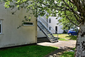 A building with a staircase leading to an upper floor, a small window, and a tree in the foreground.