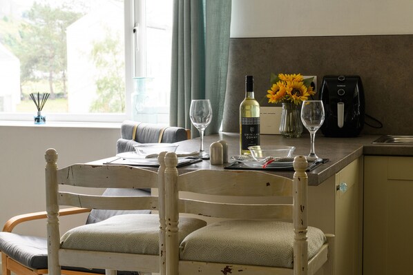 A dining area with a table set for two, a wine bottle, two glasses, and a vase with sunflowers. - Golygfa o'r Castell - Castle Views (Harlech)