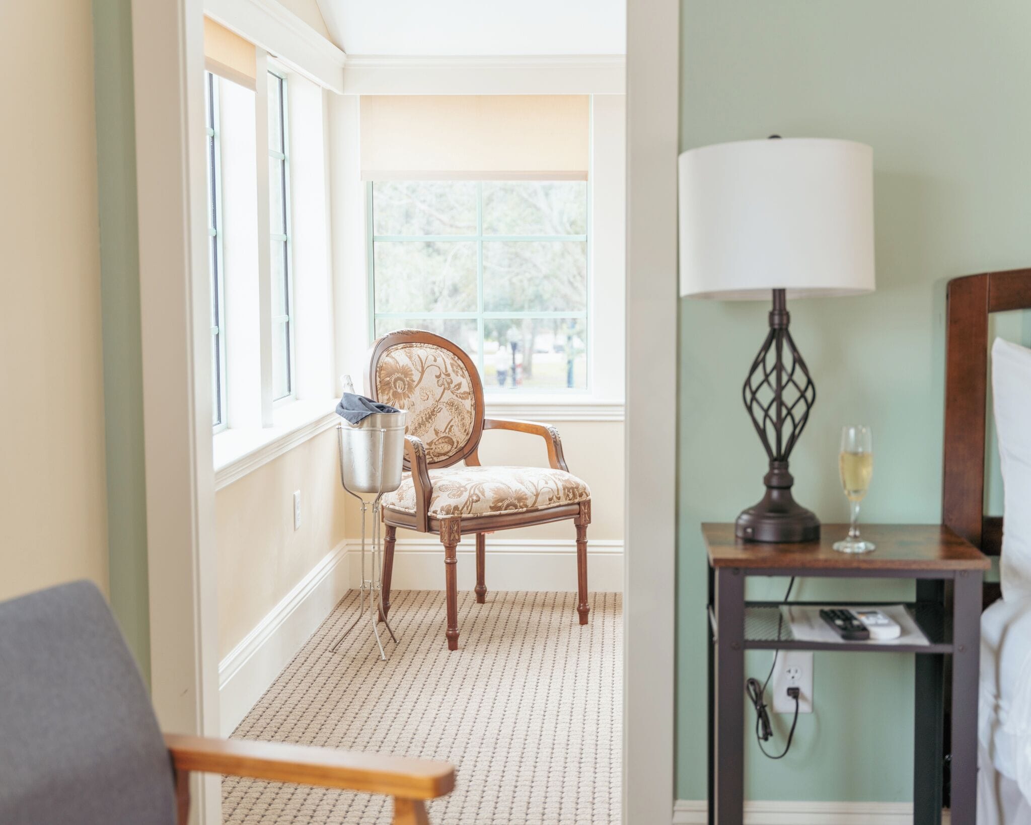 Et hotelværelse med en træstol, et lille bord med en lampe og udsigt til det fri gennem et vindue.