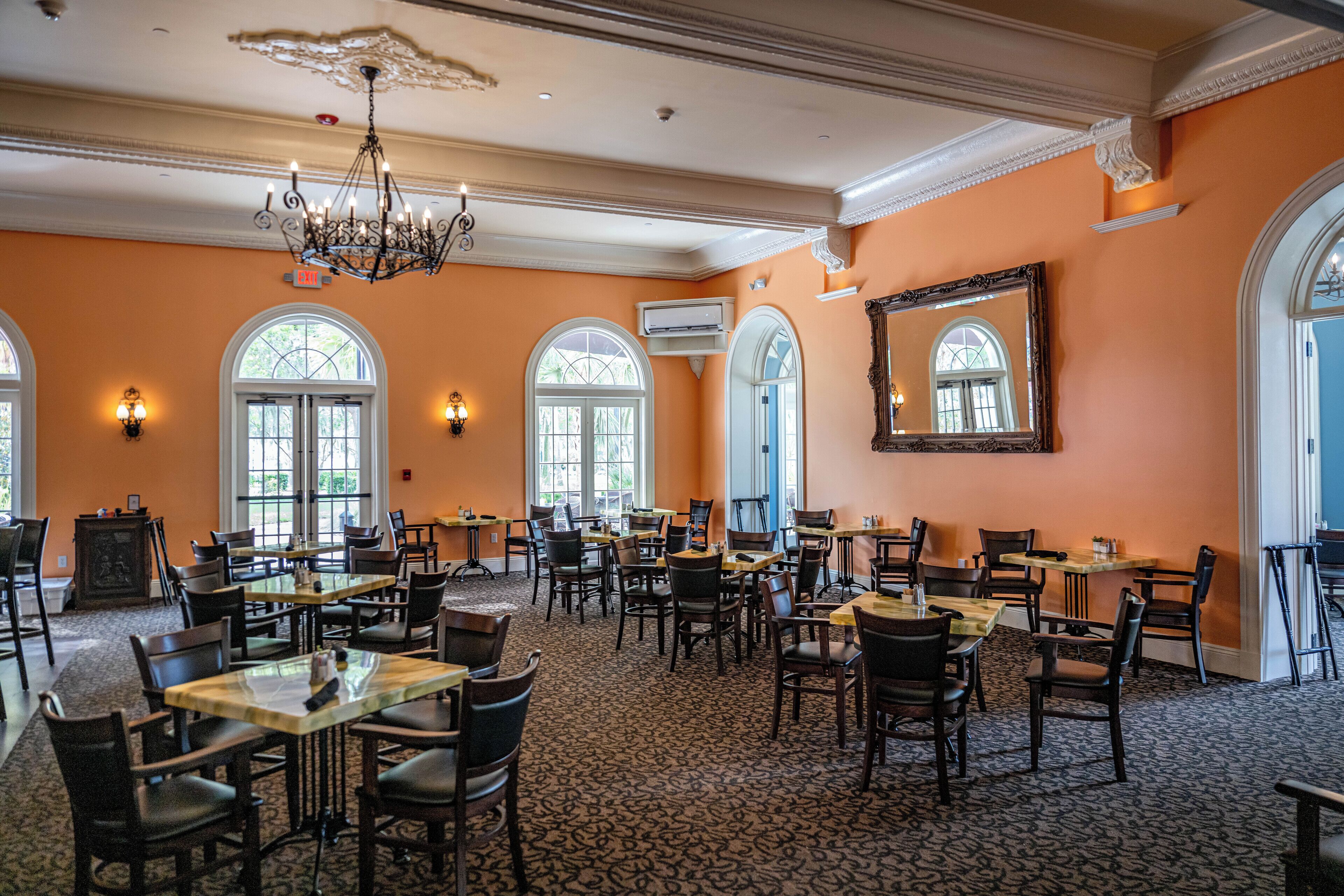 A spacious dining area with multiple tables and chairs, large windows, and a chandelier.