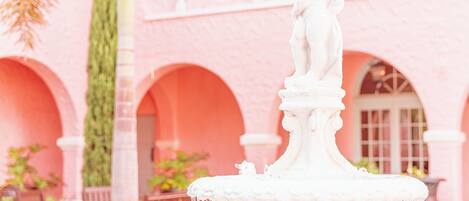 A pink building with arched windows and a statue on a fountain.