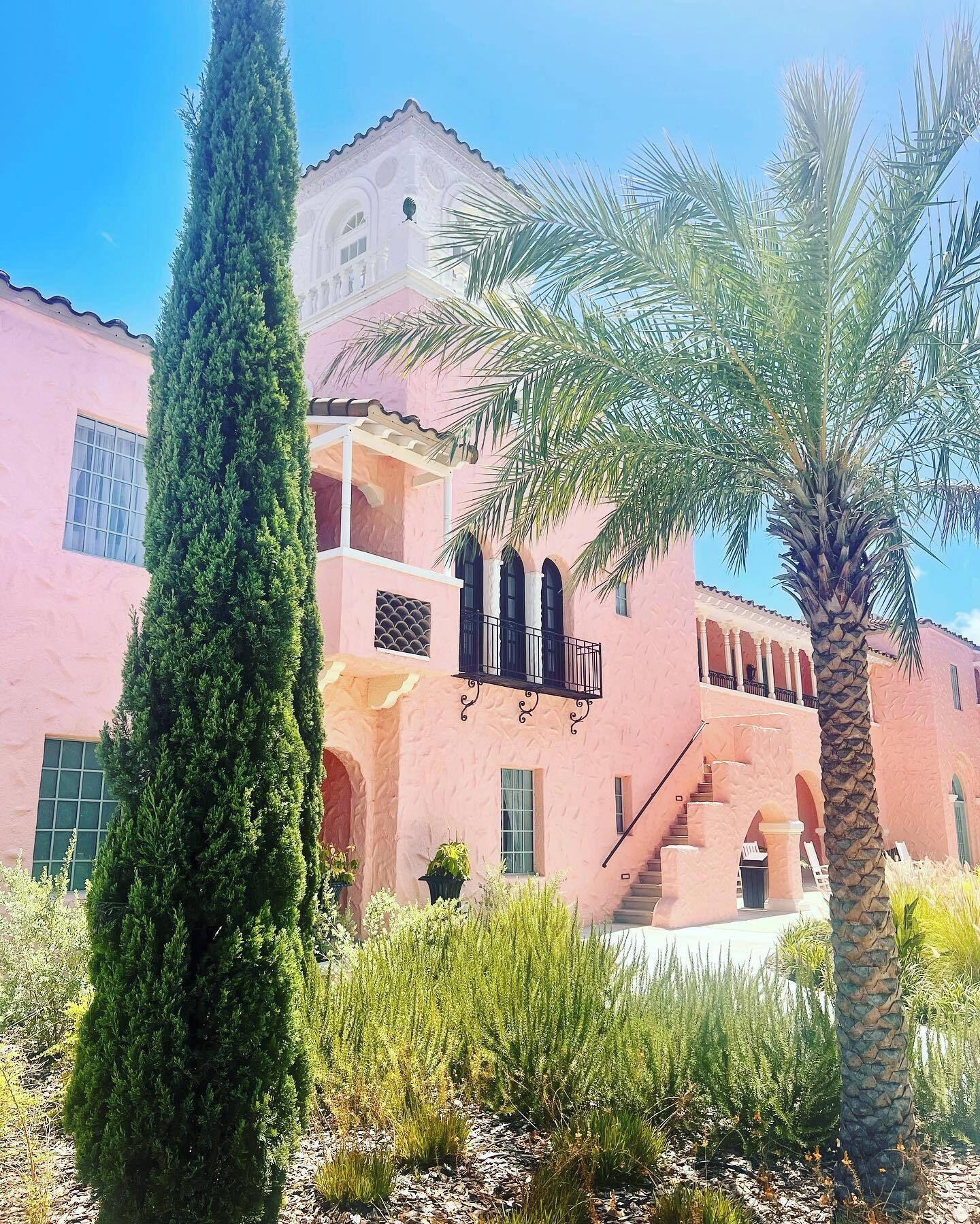 Un edificio rosa con balcón, palmeras y una escalera que lleva a un nivel superior.