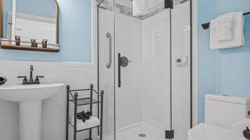 Une salle de bain avec un lavabo blanc, une douche à parois de verre, des toilettes et un porte-serviettes.