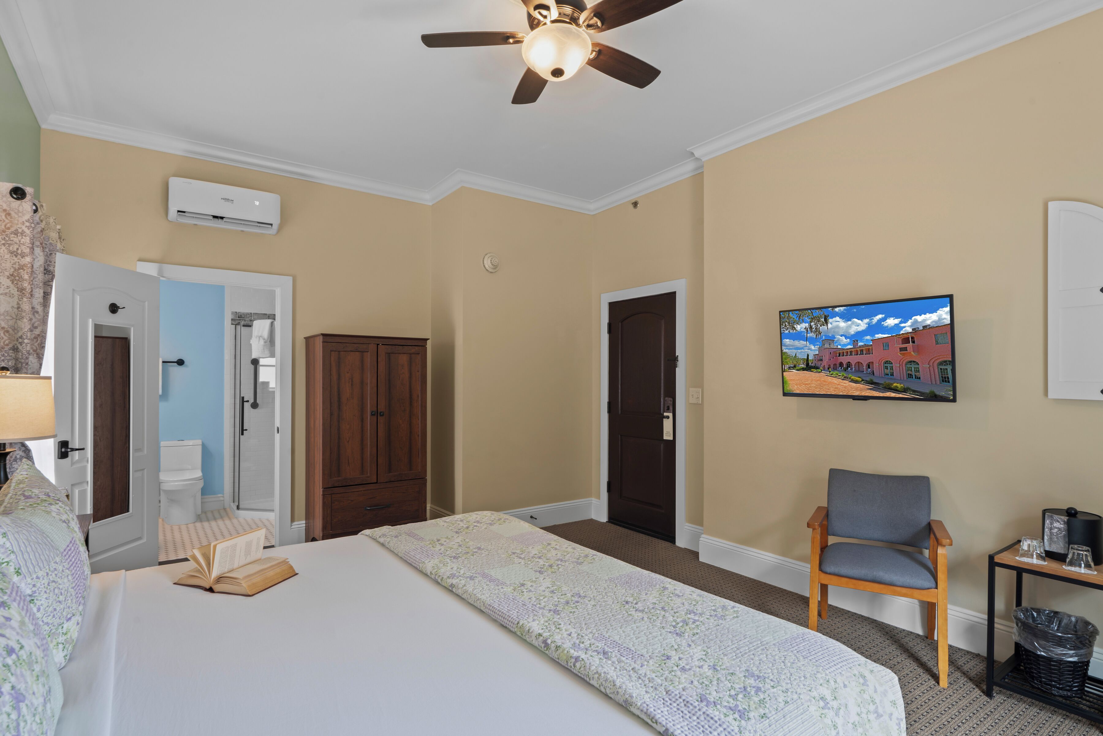 A hotel room with a bed, a chair, a TV, and an air conditioning unit.