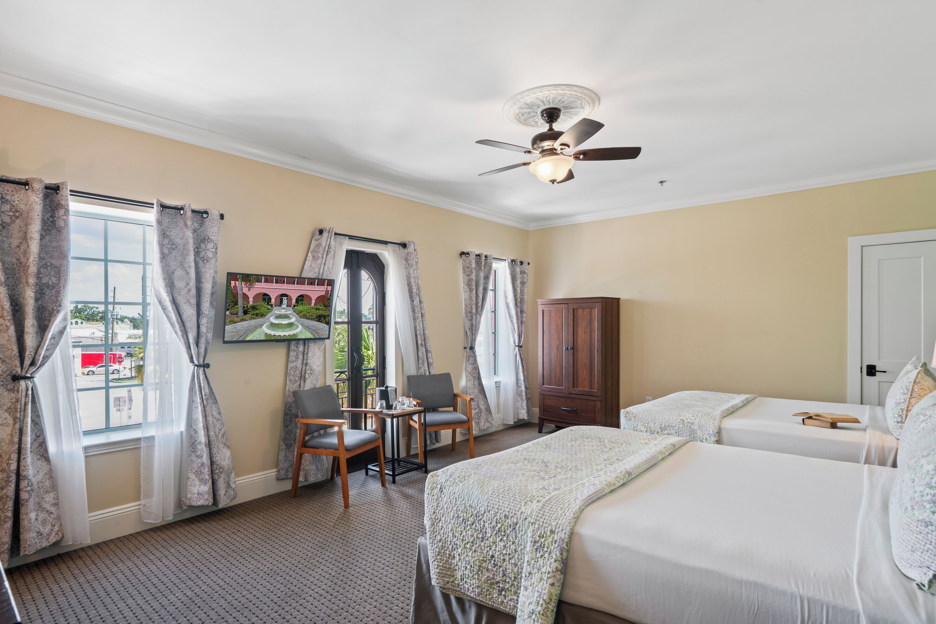 A hotel room with two beds, a ceiling fan, a wooden cabinet, and a table with chairs.