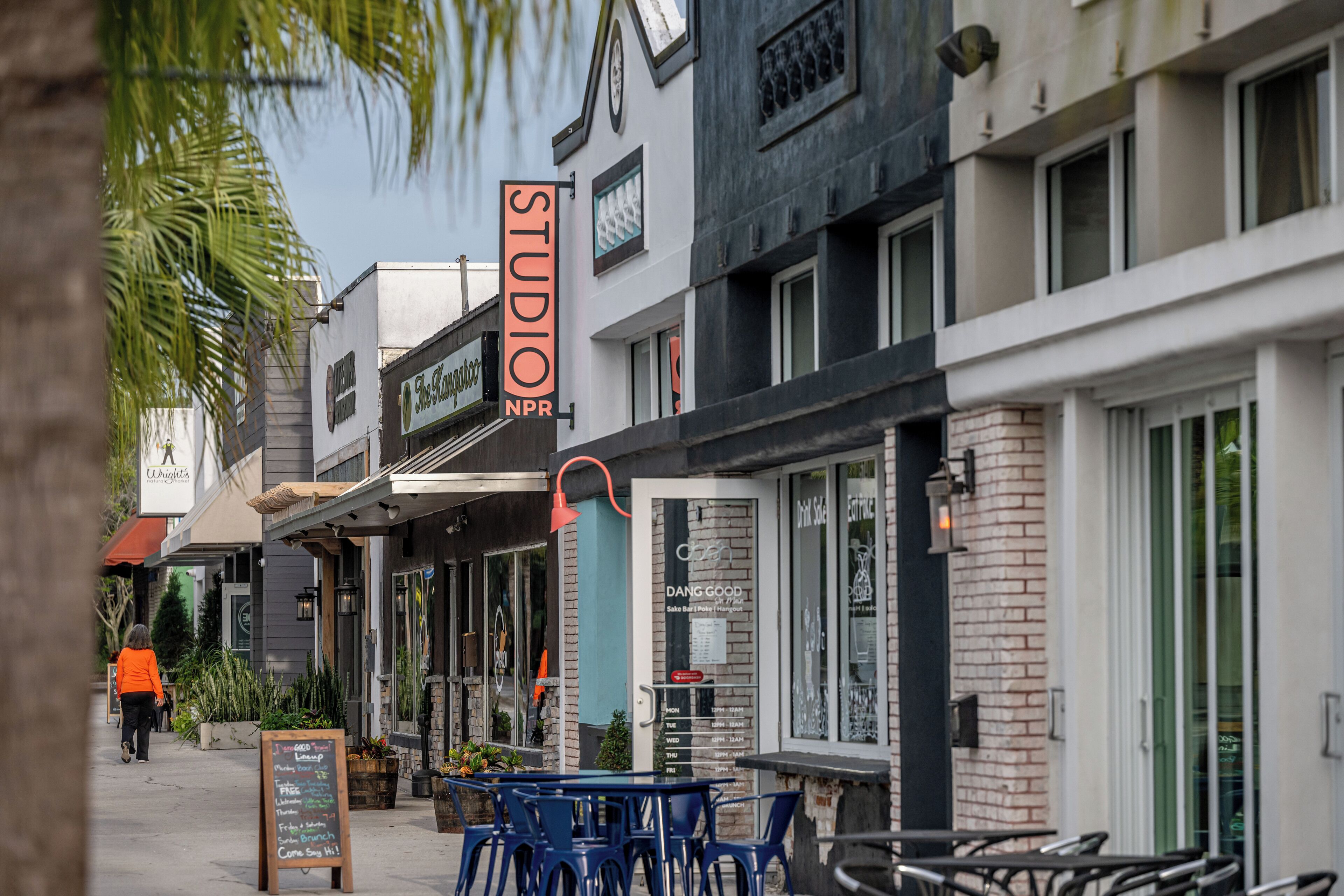 Une vue de rue avec un bâtiment portant l’inscription « STUDIO APP » et des sièges extérieurs avec des chaises bleues.