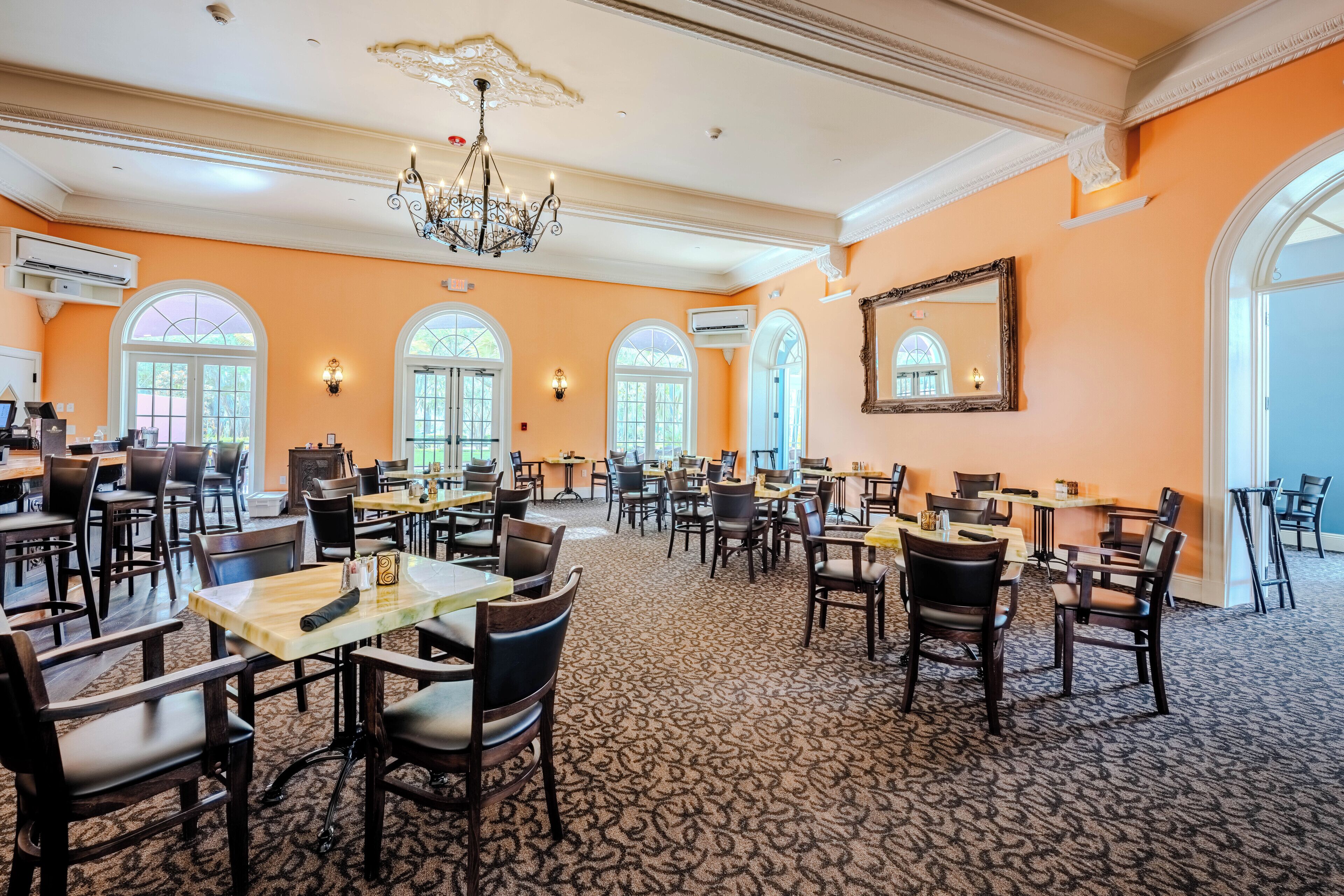 A spacious dining area with multiple tables and chairs, large windows, and a chandelier.