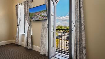 A room with a large window, a mounted TV, patterned curtains, and a view of a street and buildings.