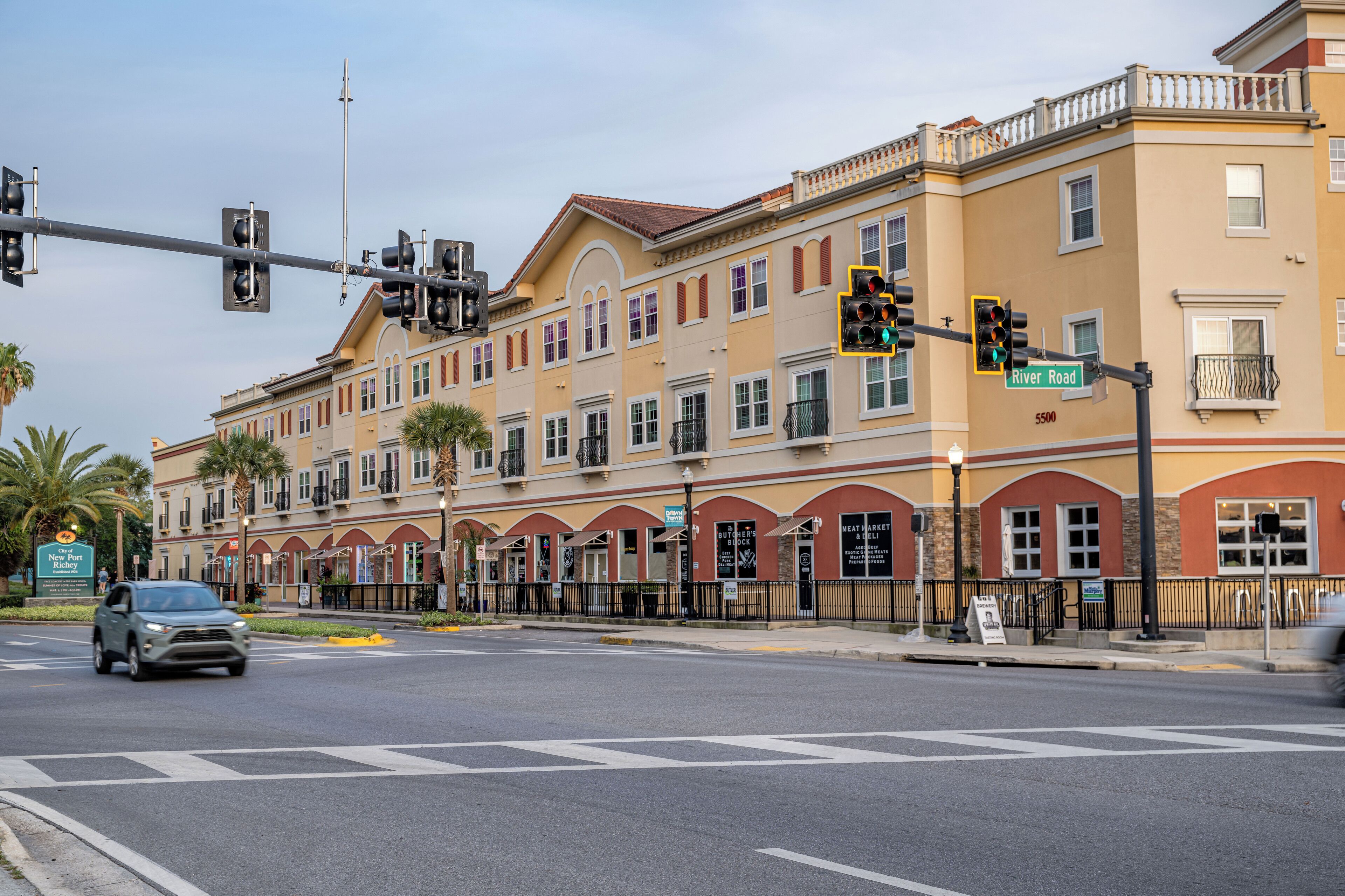 A multi-story building with a yellow facade and arched windows, located at a street corner with traffic lights and a crosswalk.