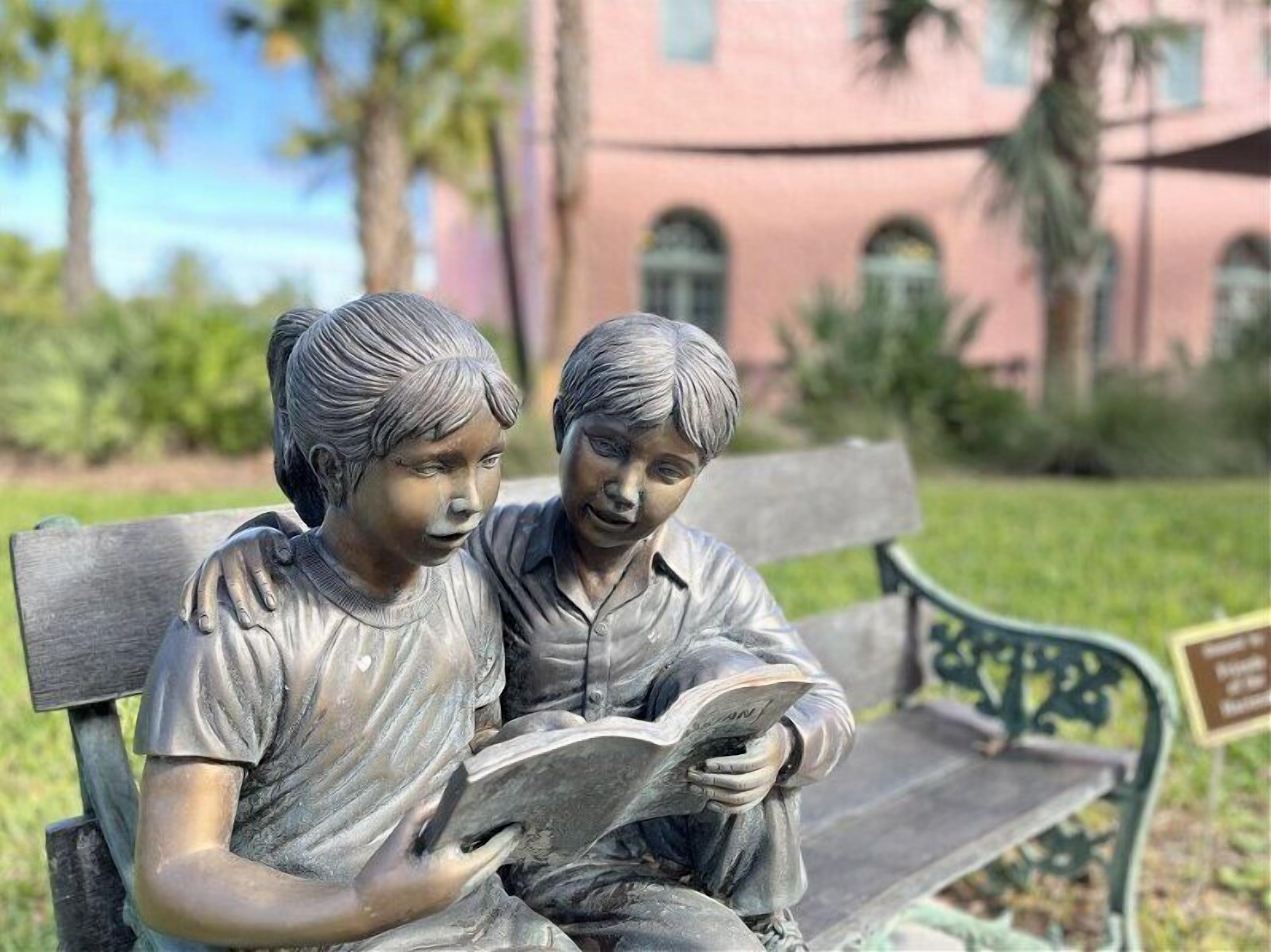Una statua raffigura due bambini seduti su una panchina e che leggono un libro.