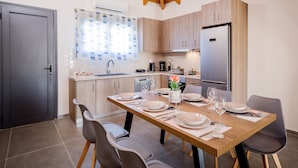 A modern kitchen with wooden cabinets, a stainless steel refrigerator, and a dining table set for four. - Aurelia Villa (Zakynthos)