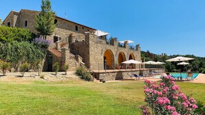 Un edificio in pietra con area piscina, inclusi lettini e ombrelloni.