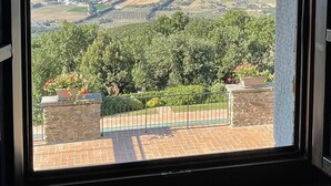 Ampia finestra con vista su un paesaggio costiero, campi e montagne in lontananza.