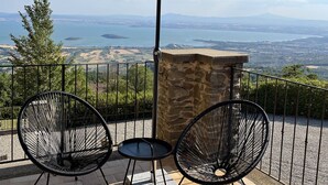 Un patio con due sedie nere in filo di ferro, un piccolo tavolo rotondo e un ombrellone verde. Il patio si affaccia su una vista panoramica di un lago e montagne lontane.