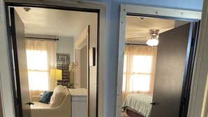 A hallway leading to a bedroom with a bed, a nightstand, and a window with curtains. - Family suite sleeps 11!  We are near Champaign-Urbana 4 bedrooms & 2.5 bathrooms (Saint Joseph)