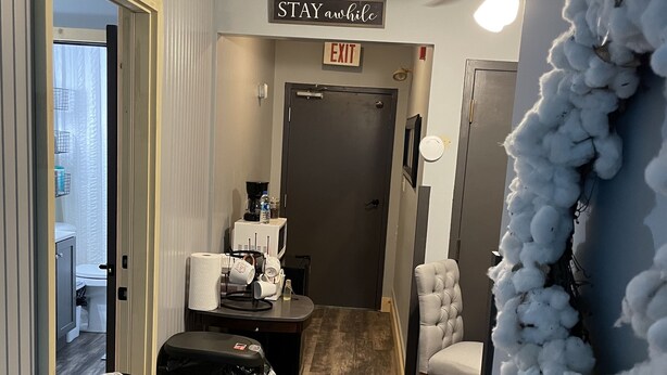 A hotel hallway with a sign reading "STAY awhile," a trash bin, a coffee station, a door marked "EXIT," and a chair. - Family suite sleeps 11!  We are near Champaign-Urbana 4 bedrooms & 2.5 bathrooms (Saint Joseph)
