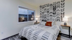 A hotel room with a bed, two bedside tables, a window, and a patterned headboard.