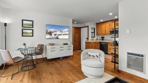 Une cuisine moderne avec des meubles en bois, un coin repas doté d’une table ronde et de chaises, et une grande fenêtre offrant une vue sur les montagnes.