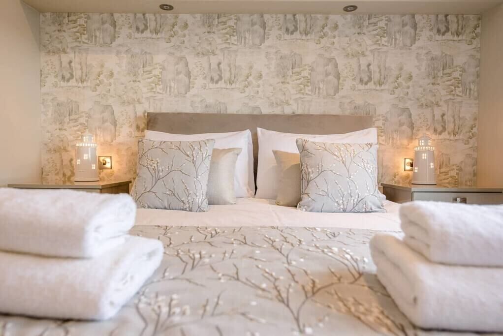 A neatly made bed with a tree-patterned bedspread, two pillows, and two bedside lamps.