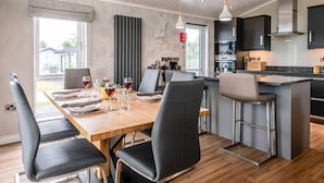 A modern kitchen with dark cabinets, a wooden island, and a dining area with a table set for four. - Marshwiggle, Aldeburgh (Aldeburgh)