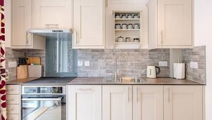 A modern kitchen with light-colored cabinets, a stainless steel sink, and a built-in oven. - Hattie's, Great Glemham (Saxmundham)
