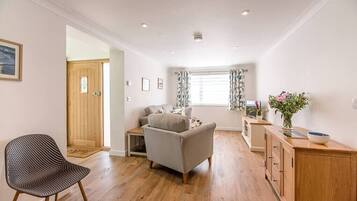 A compact living space with a wooden floor, a grey sofa, a patterned chair, and a wooden cabinet.