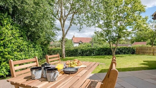 A wooden table set outdoors with a breakfast spread including croissants, fruit, and a jug of orange juice. - Hattie's, Great Glemham (Saxmundham)