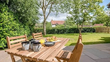 A wooden table set outdoors with a breakfast spread including croissants, fruit, and a jug of orange juice.