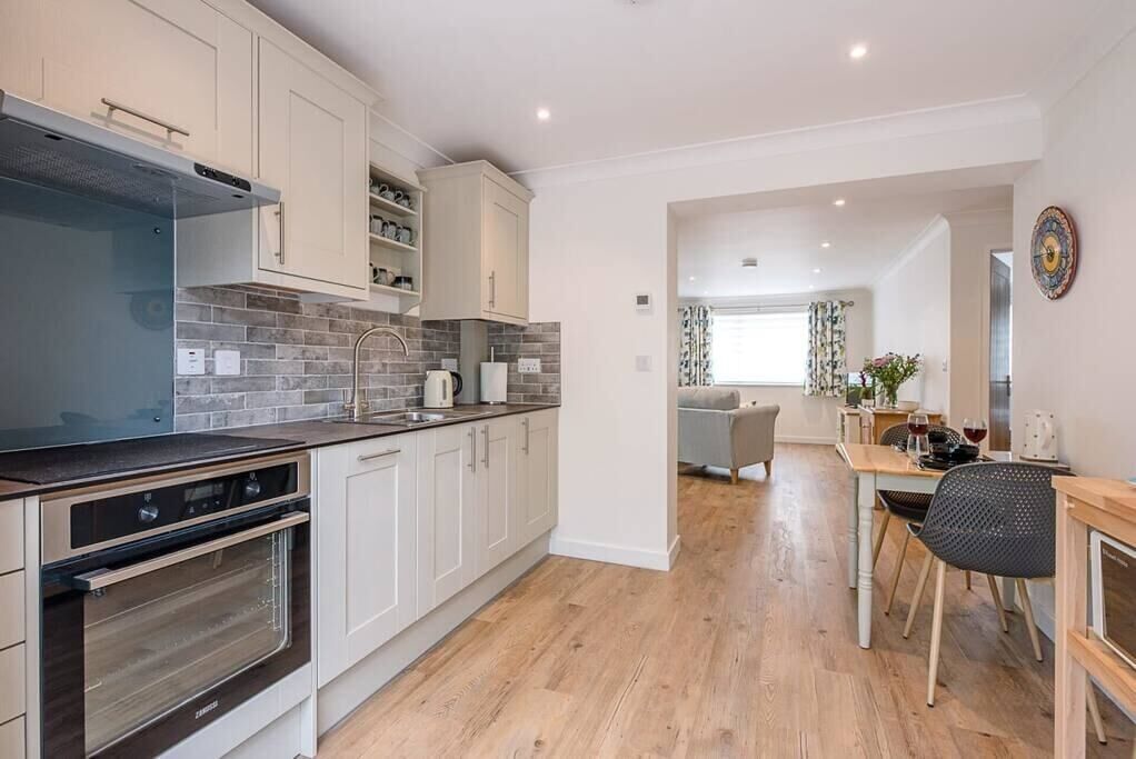 A modern kitchen with white cabinets, a built-in oven, and a dining area with a table and chairs.