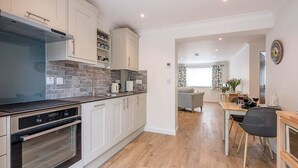A modern kitchen with white cabinets, a built-in oven, and a dining area with a table and chairs. - Hattie's, Great Glemham (Saxmundham)