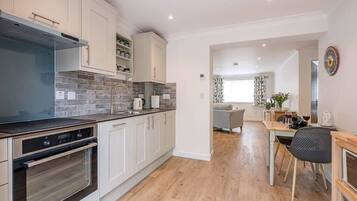 A modern kitchen with white cabinets, a built-in oven, and a dining area with a table and chairs.