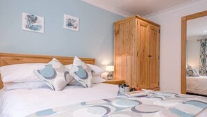 A bedroom with a bed, pillows, a nightstand, a wooden wardrobe, and two wall art pieces. - Hattie's, Great Glemham (Saxmundham)