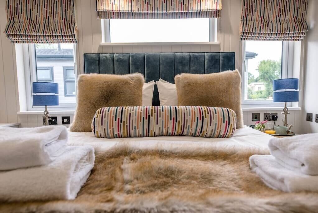 Une chambre à coucher avec une tête de lit capitonnée, deux oreillers moelleux, un oreiller à rayures et un plaid en fausse fourrure.