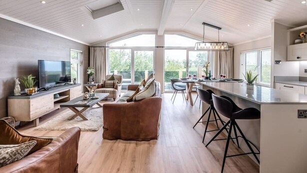 A spacious living area with a large TV, comfortable seating, a kitchen area, and large windows offering natural light and views. - Briargate, Aldeburgh (Aldeburgh)