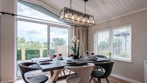 A dining area with a table set for four, large windows, and a hanging light fixture. - Briargate, Aldeburgh (Aldeburgh)