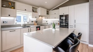A modern kitchen with white cabinetry, a central island with seating, and built-in appliances. - Briargate, Aldeburgh (Aldeburgh)