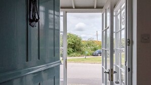 A view through a door into a parking area with a car and greenery visible outside.