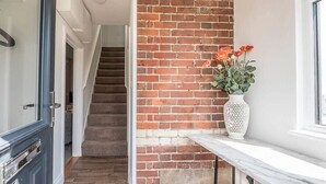 A staircase leading to a room with a brick wall and a white vase with flowers on a marble ledge.