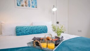 A neatly made bed with a blue blanket, a tray with breakfast items, and a small potted plant.