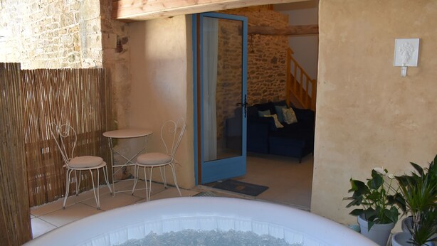 Un jacuzzi en una habitación rústica con paredes de piedra, techo de madera y una puerta azul que da a una sala de estar con sofá y una escalera.