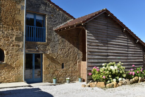 A rustic stone building with a wooden extension, a blue-framed window, and a gravel driveway.