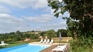 Una piscina con sillones blancos y una terraza de madera.