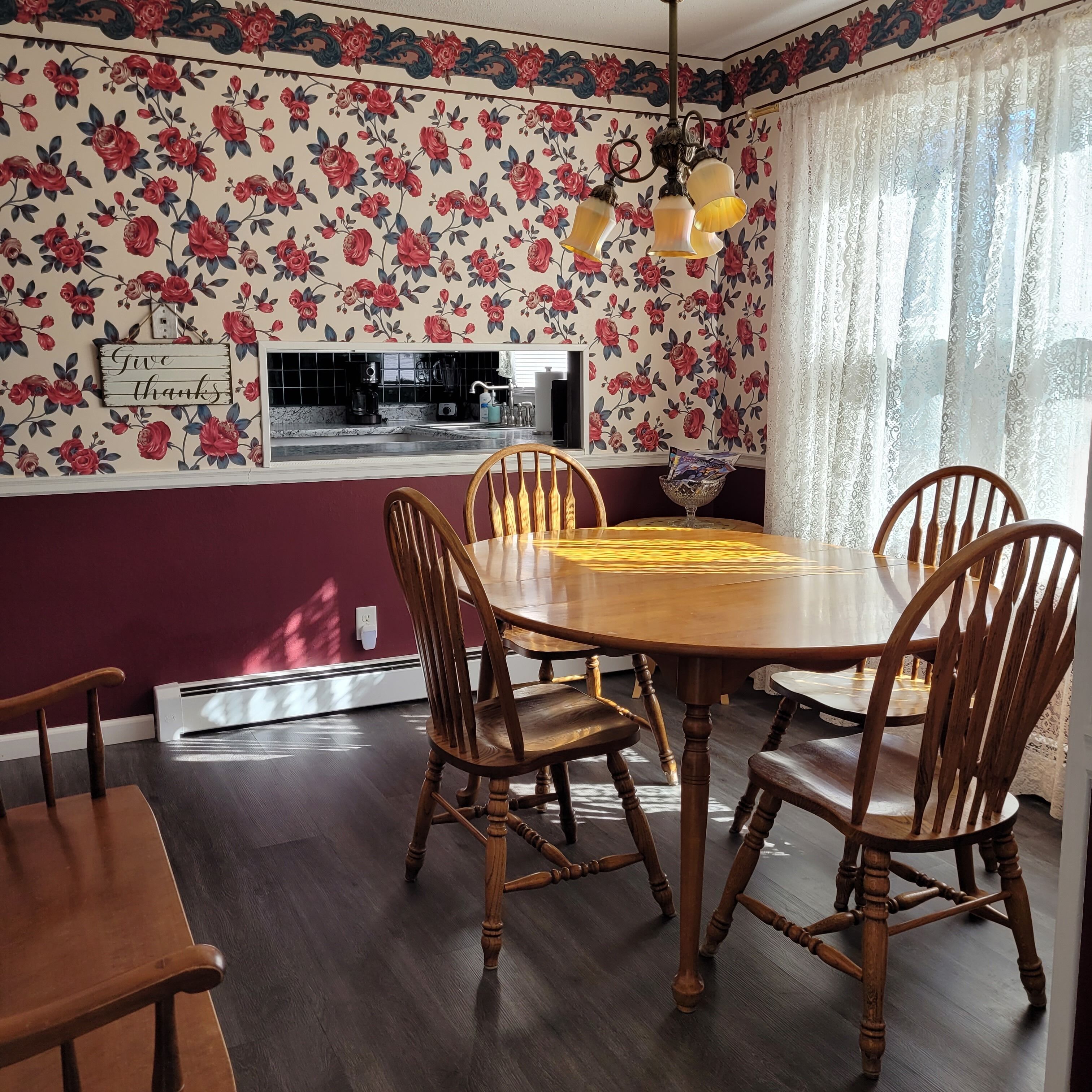 Un comedor con papel tapiz floral, una mesa redonda de madera y seis sillas de madera.