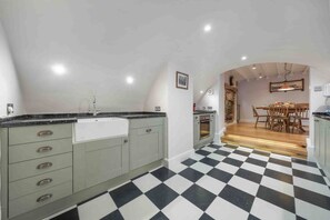 Une cuisine avec un carrelage à motifs, un coin repas avec une table et des chaises en bois, et une cheminée en briques.